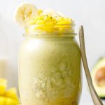 Mango and avocado smoothie in glass with spoon resting on side