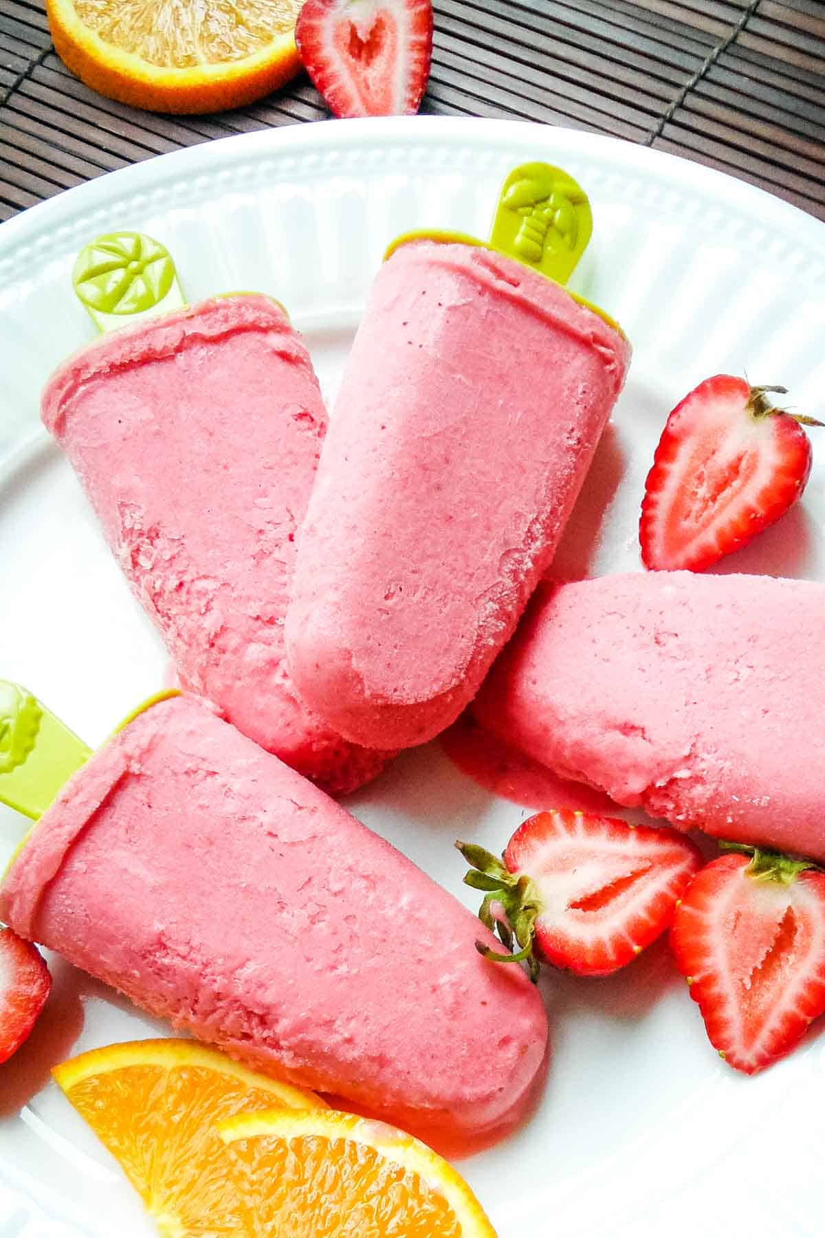 Strawberry cream popsicles on white plate with fruit