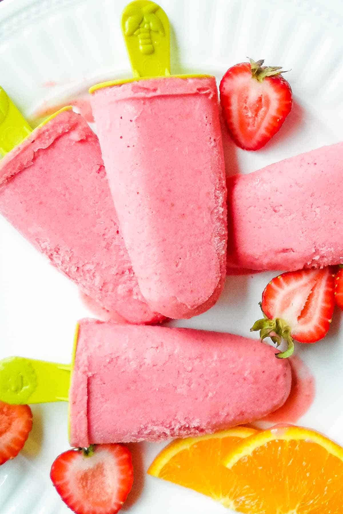 strawberries and cream popsicles on plate with fresh strawberry and orange slices