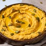 Pumpkin Hummus in brown pottery serving bowl topped with toasted pumpkin seeds