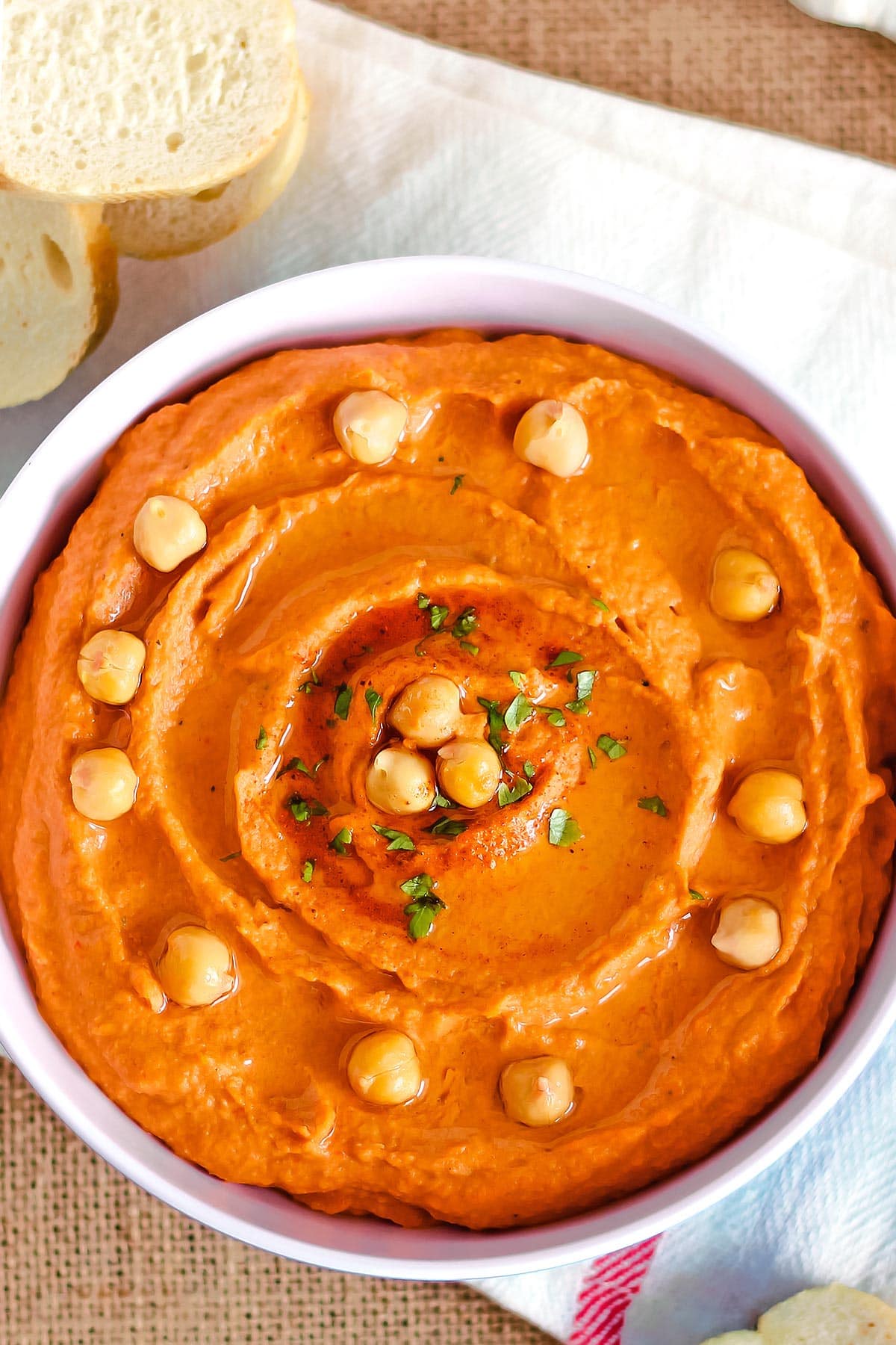 Bowl of red pepper hummus with bread slices on side