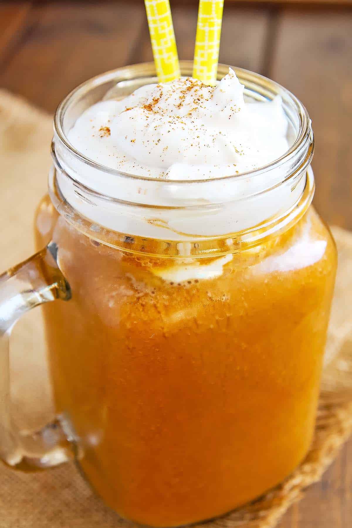 starbucks pumpkin spice frappuccino blended drink in mason glass with whipped cream topping and yellow straws