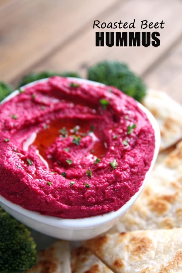pink roasted beet hummus in small white bowl with pita triangles and broccoli florets