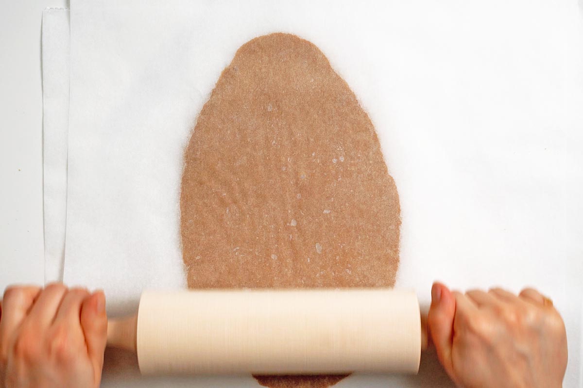 Rolling pin on German gingerbread cookie dough between parchment sheets