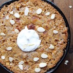 gluten free apple skillet cake in cast iron pan with sliced almond and whipped coconut cream topping
