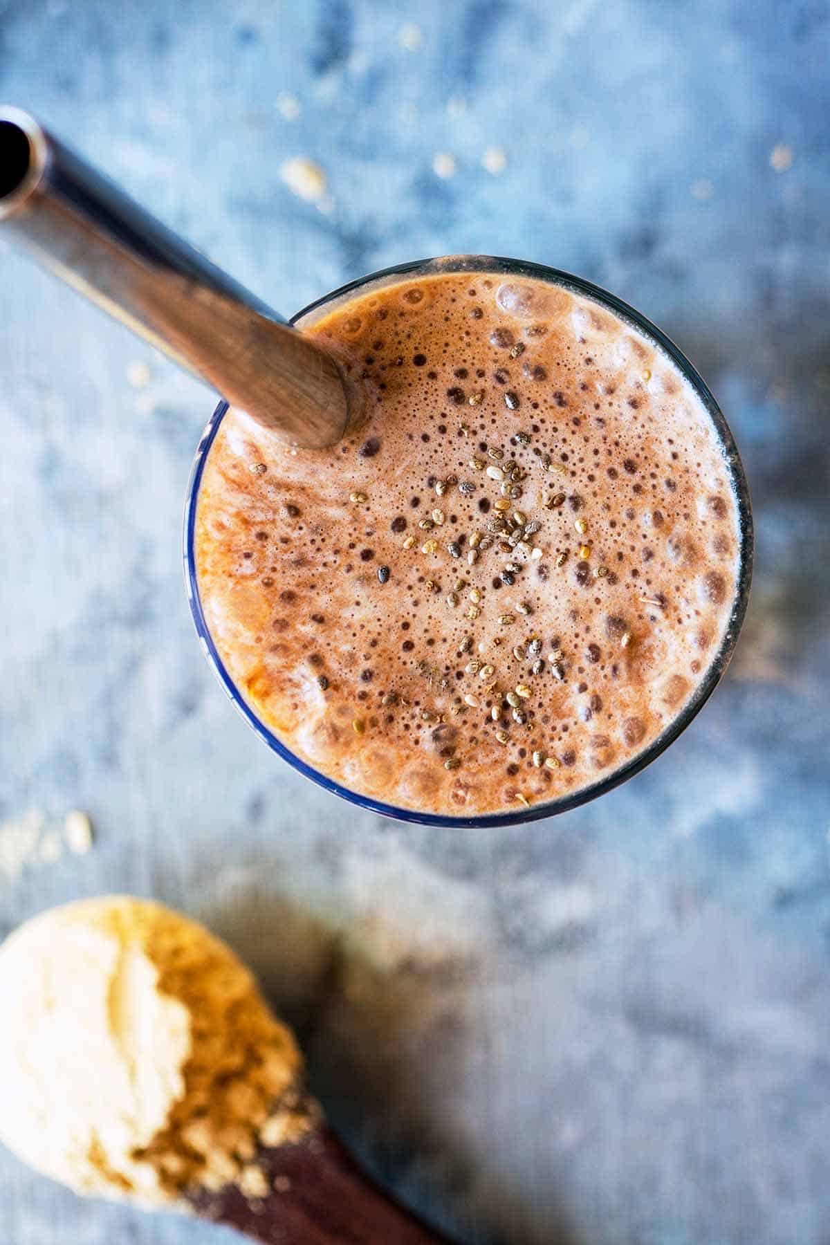 top down view into glass filled with chocolate protein shake with chia topping and thick metal straw
