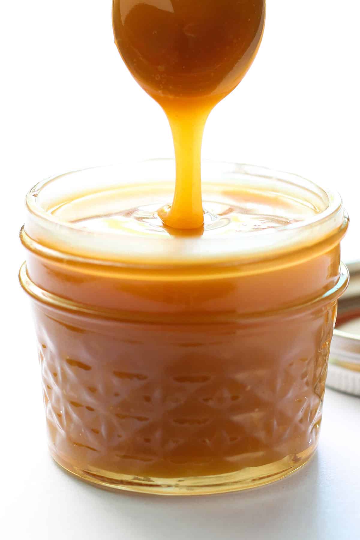 caramel sauce drizzling off a spoon into small jar