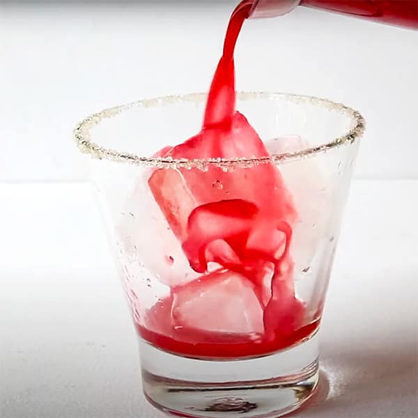 pink drink pouring from cocktail shaker into glass with ice