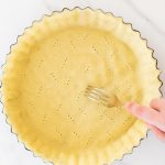 Fork pricking all butter pie dough in pan