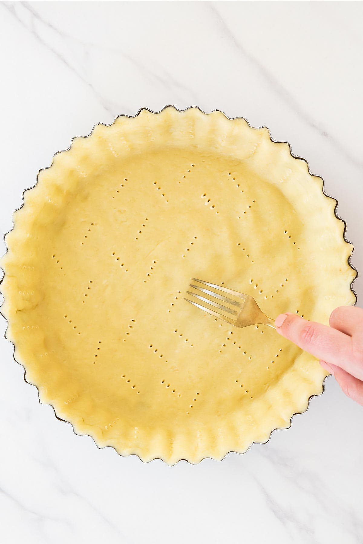 Fork pricking all butter pie dough in pan