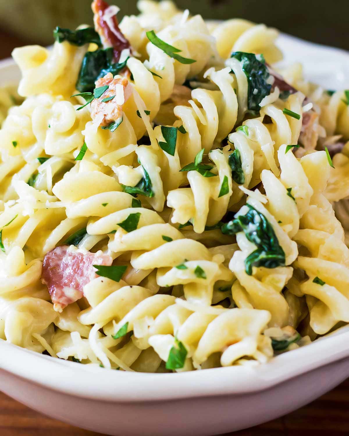 Spiral pasta with creamy bacon spinach sauce in bowl