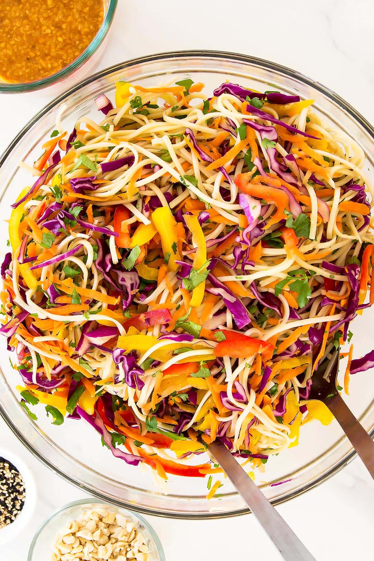 Tossed veggie noodles salad in bowl with serving tongs