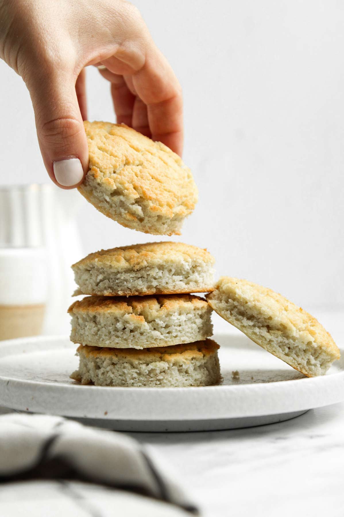 Hand taking one from a stack of coconut flour biscuits on small white plate