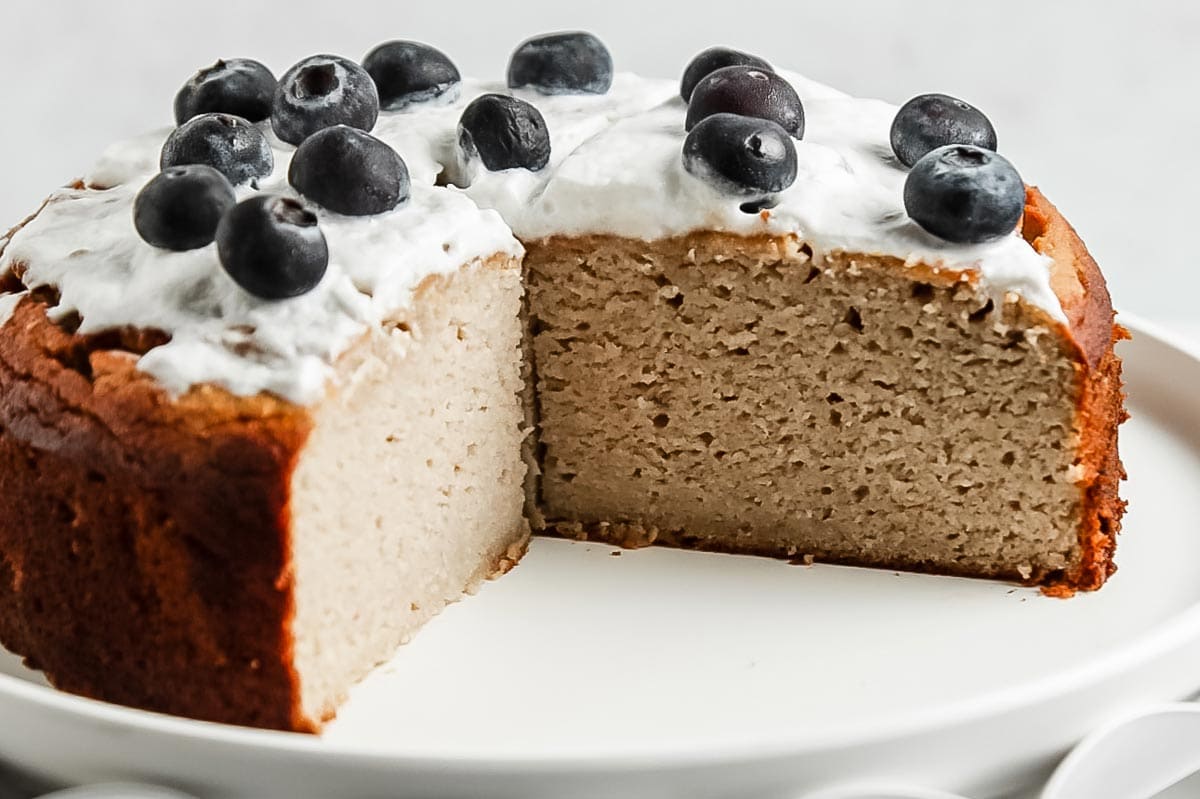 Close up of cut coconut flour banana cake on cake stand with frosting and blueberries on top