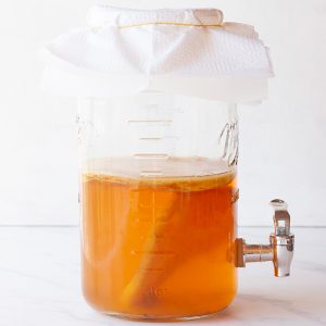 Large gallon dispenser jar with kombucha brew, scoby, covered with paper towel