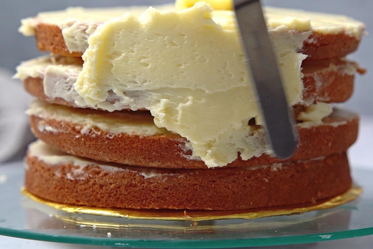 spatula spreading Swiss meringue frosting on layer cake