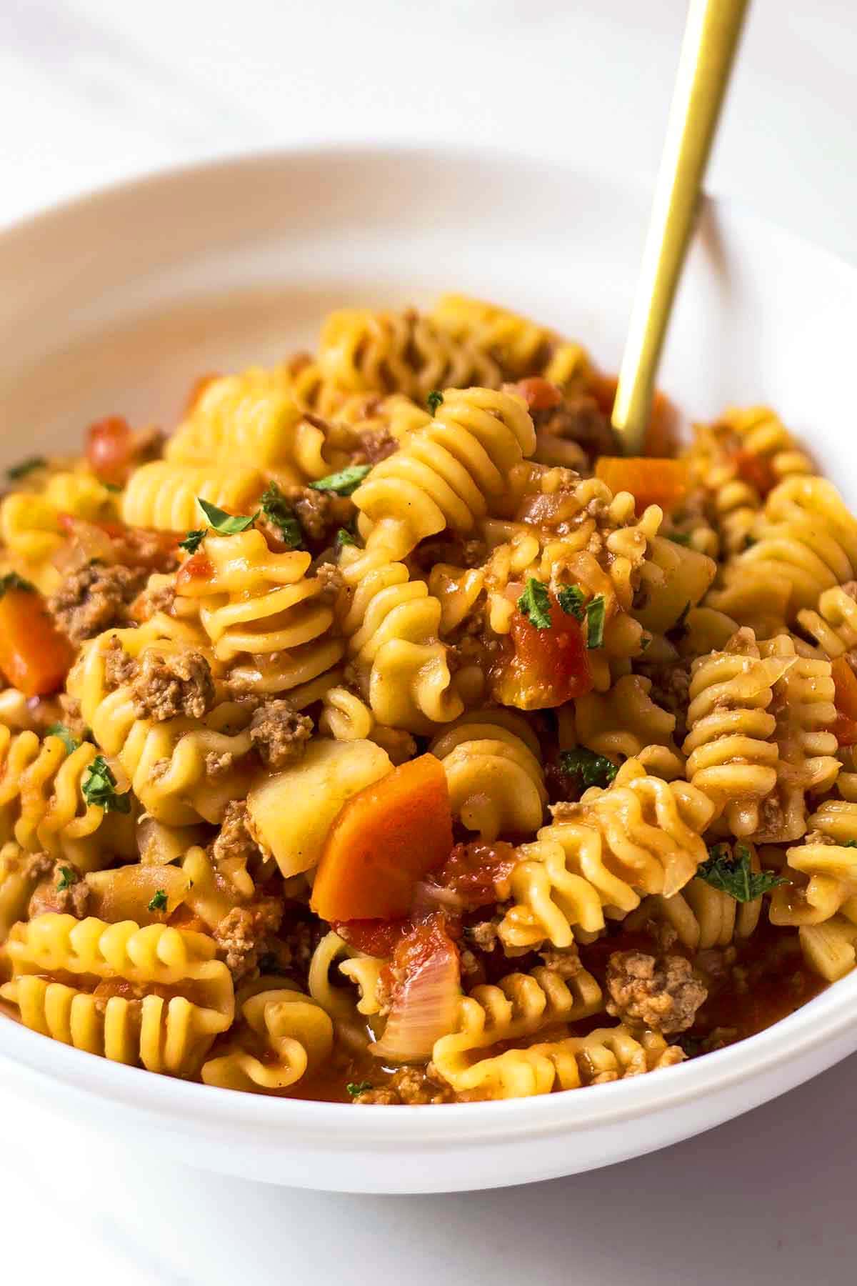 Ground Beef Pasta Stew in white bowl with golden fork sticking out