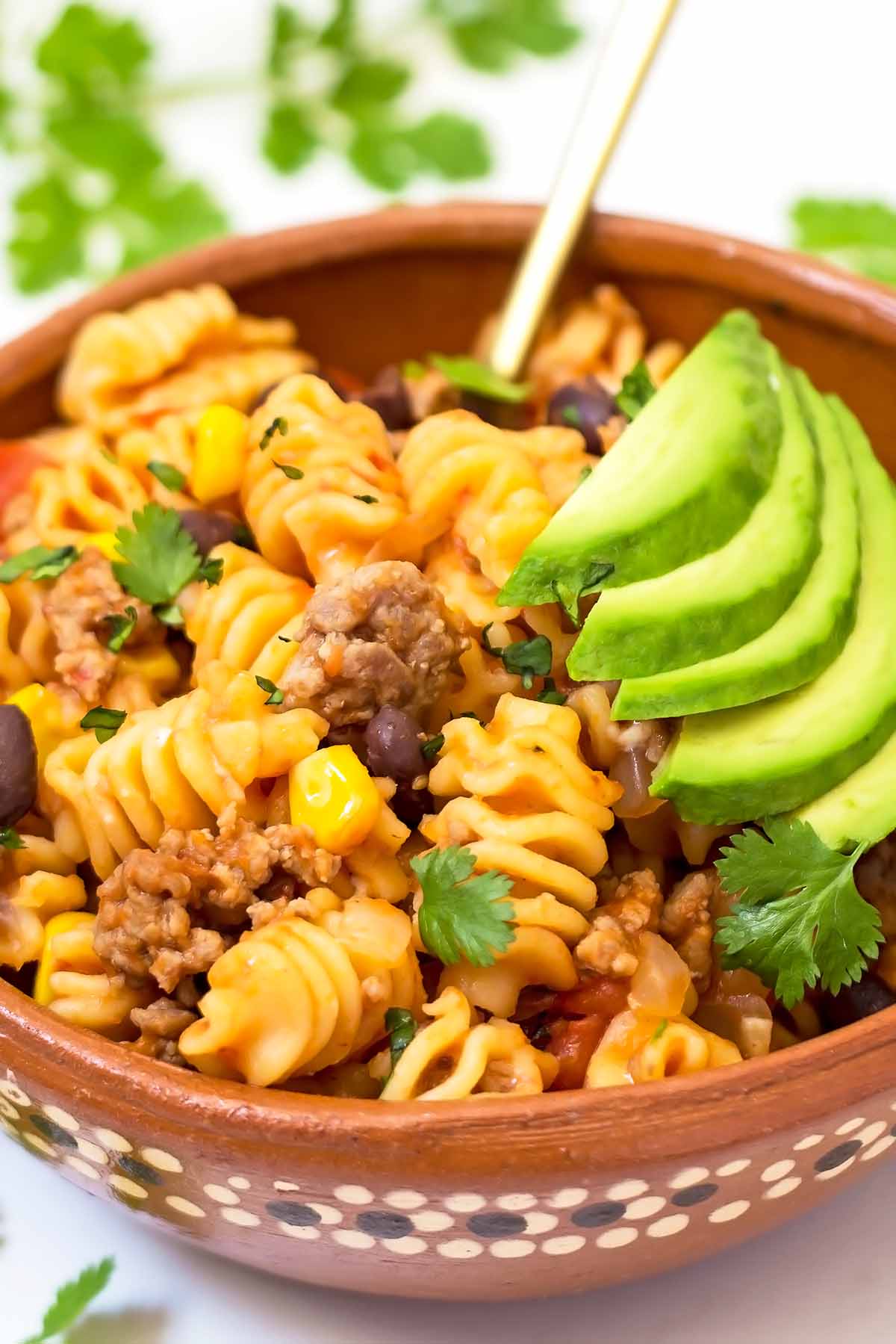 one pot taco pasta in Mexican clay bowl with sliced avocado topping