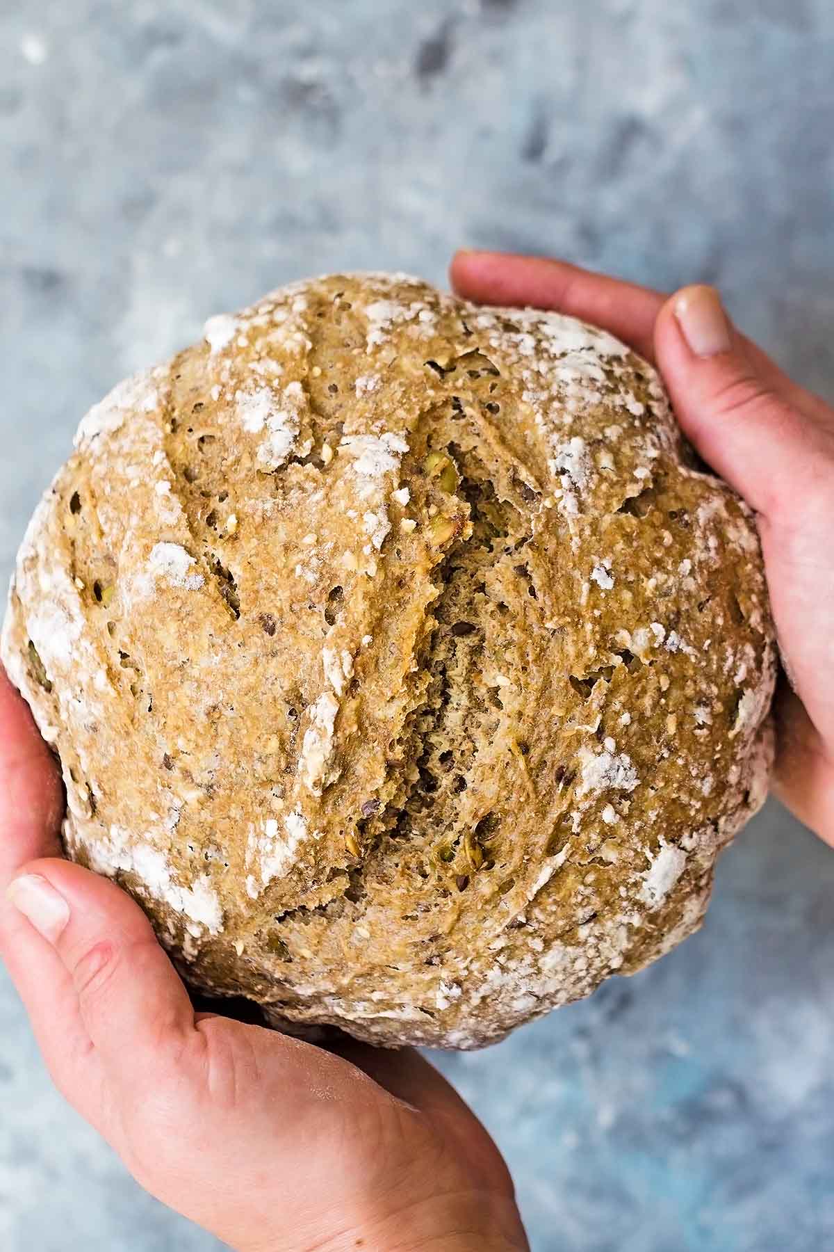 Hands holding seeded sourdough bread loaf