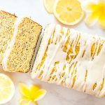 Coconut Flour Lemon Loaf with 2 loaf slices, lemon slices, and white and yellow flowers