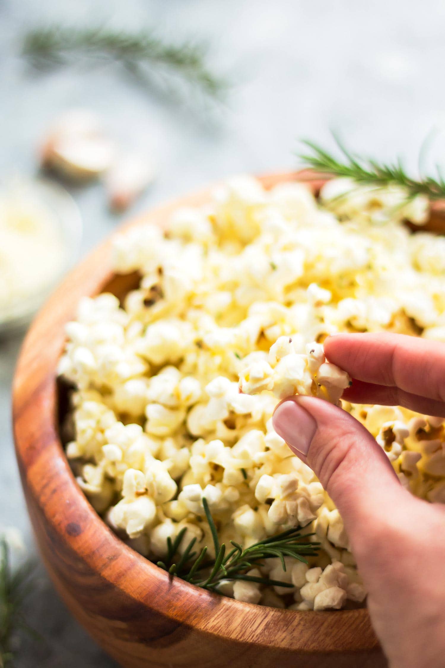 Hand holding a piece of garlic parmesan popcorn with full popcorn bowl in background