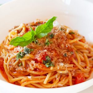white bowl with plated cooked spaghetti and tomato meat sauce