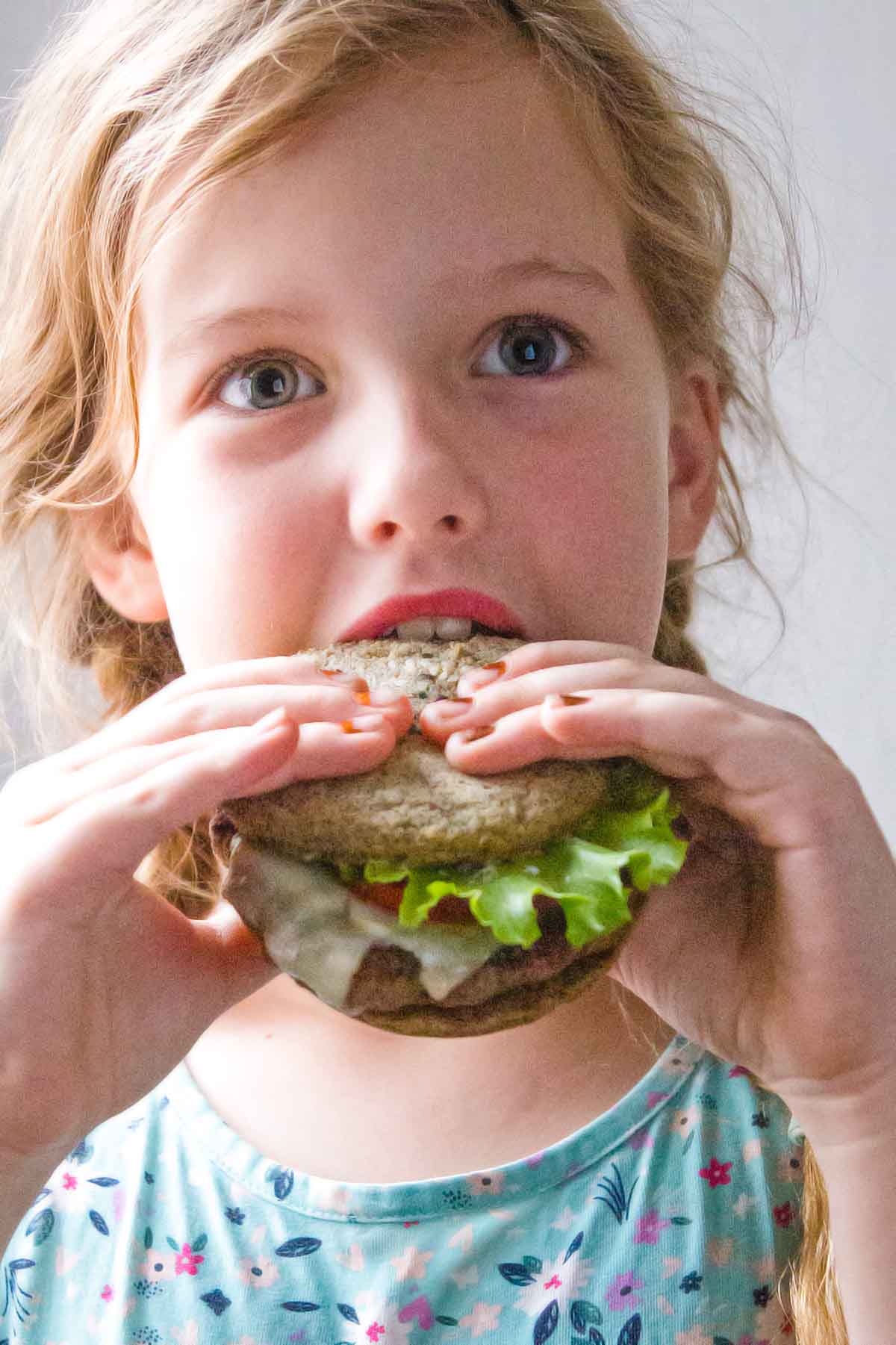Girl biting into hamburger with keto bread rolls made with coconut flour
