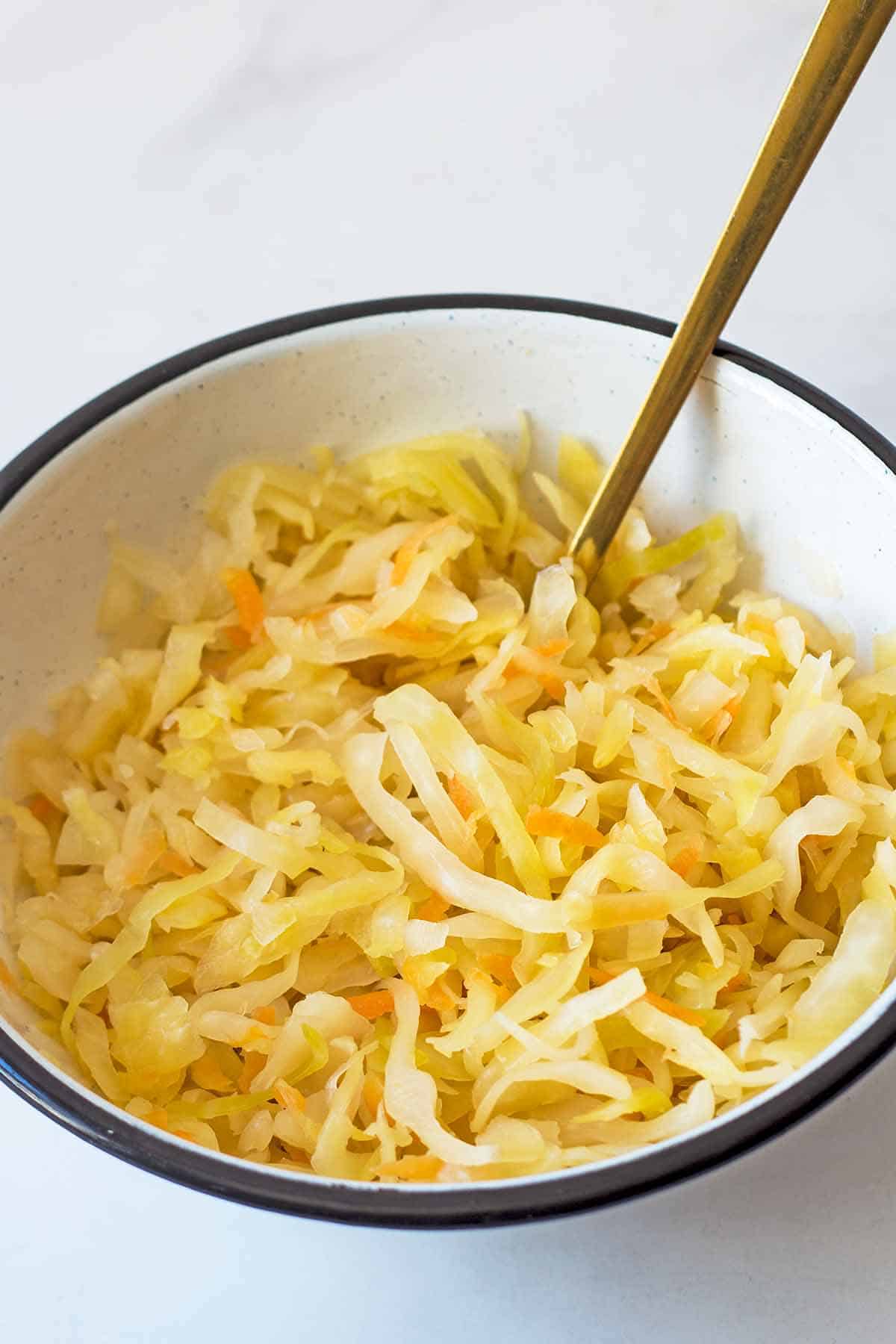 Homemade sauerkraut in white serving bowl with golden fork