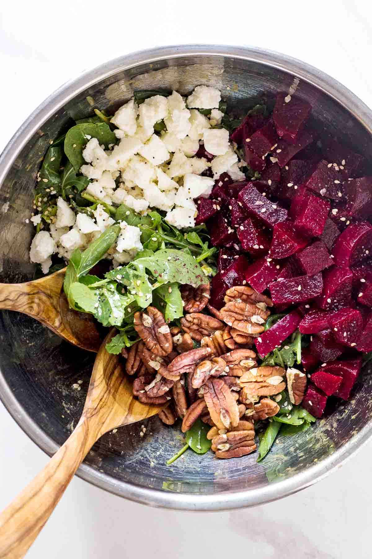 arugula beet salad ingredients in one large bowl with 2 wooden serving utensils