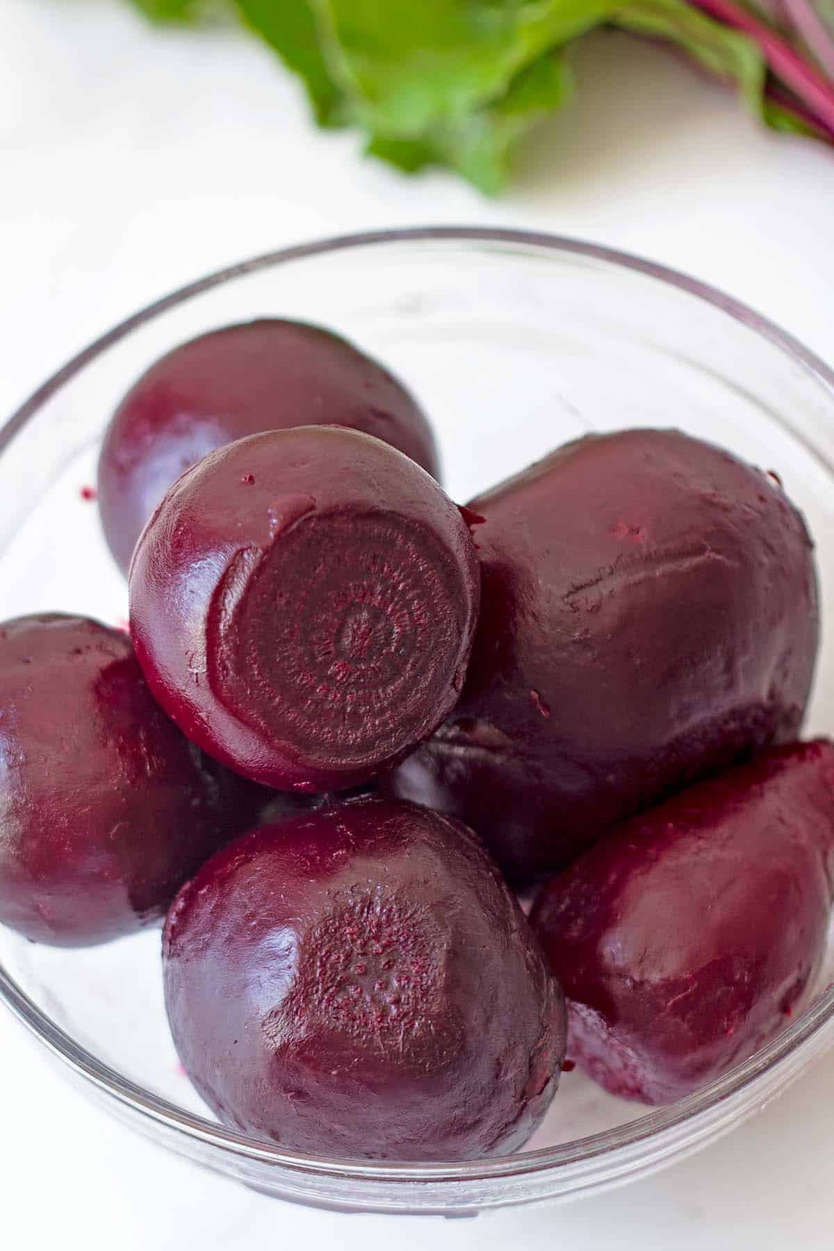 glass bowl of small cooked beets with raw beet greens in background