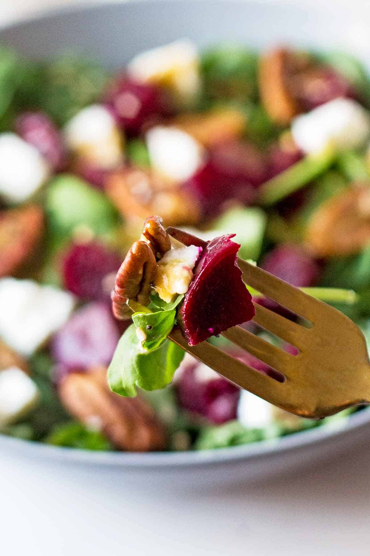 fork with arugula, beet, pecan, and goat cheese  piece over a full salad plate in background