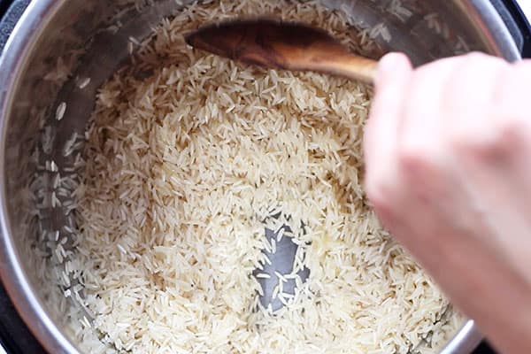 hand stirring rice in instant pot with wooden spoon