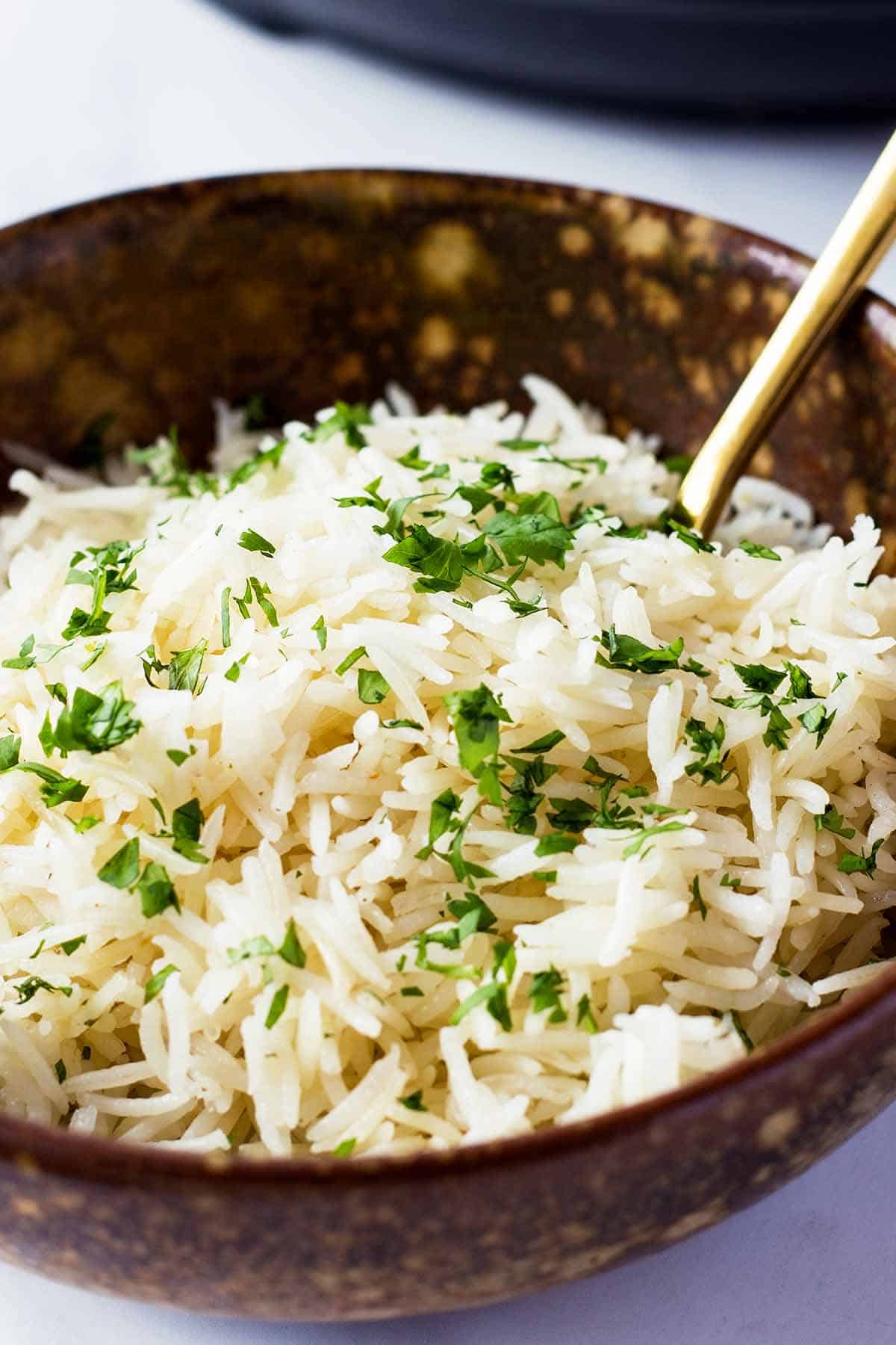 brown ceramic bowl with instant pot white rice, chopped parsley topping, and golden fork 