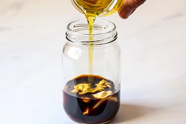 olive oil being poured into small glass jar with other ingredients for balsamic mayo dressing