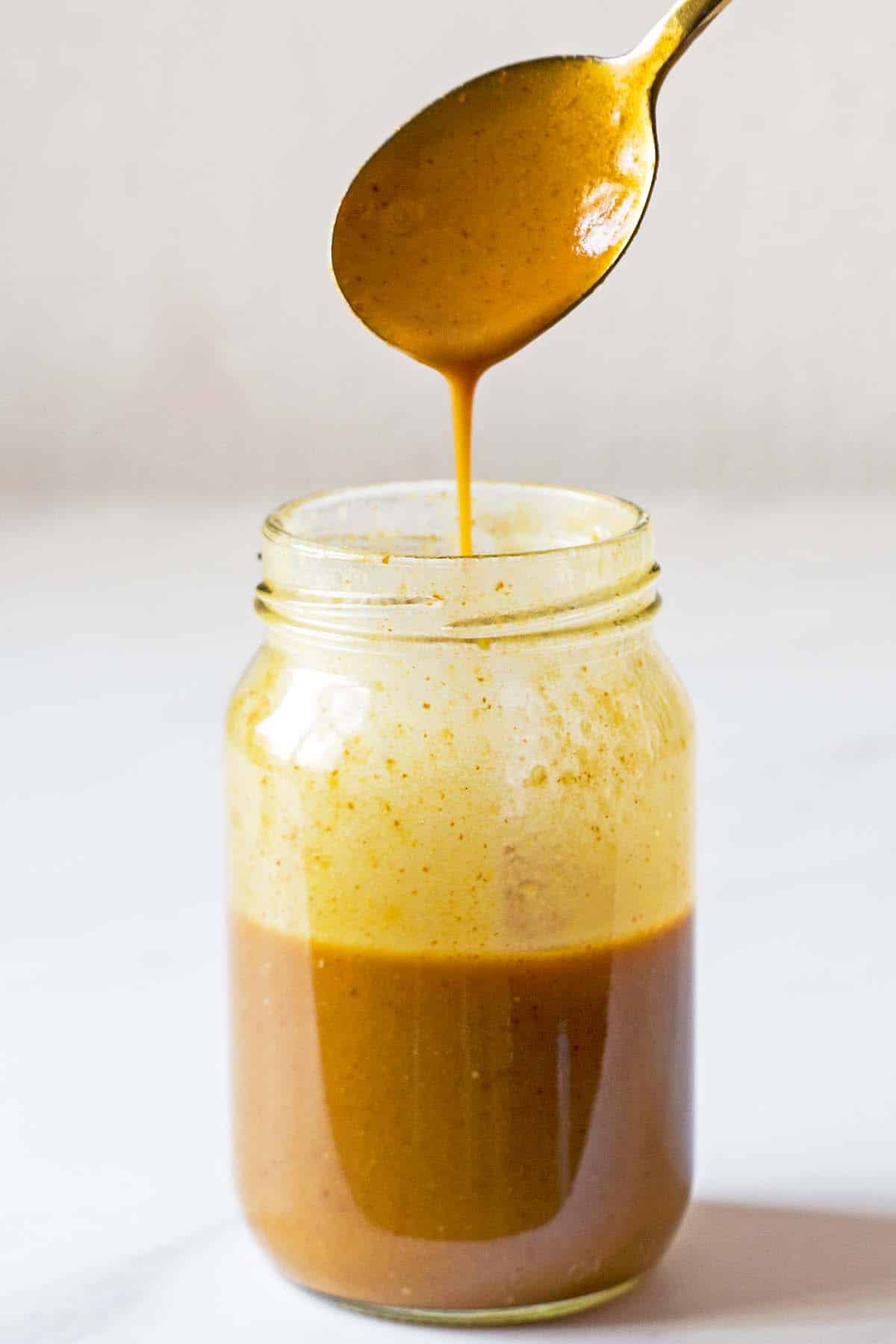 creamy balsamic dressing in glass jar golden spoon drizzling dressing