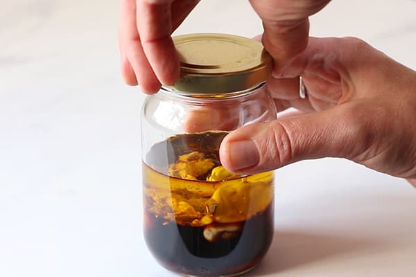 hand closing golden lid on glass jar with salad dressing ingredients