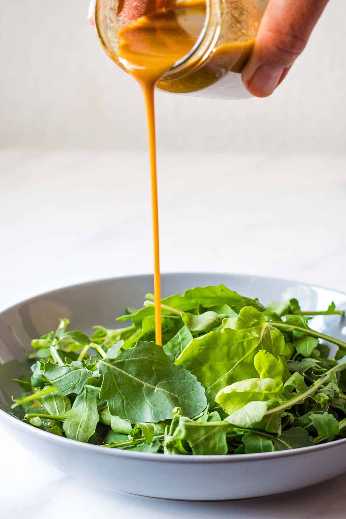 homemade balsamic dressing being drizzled on arugula leaves