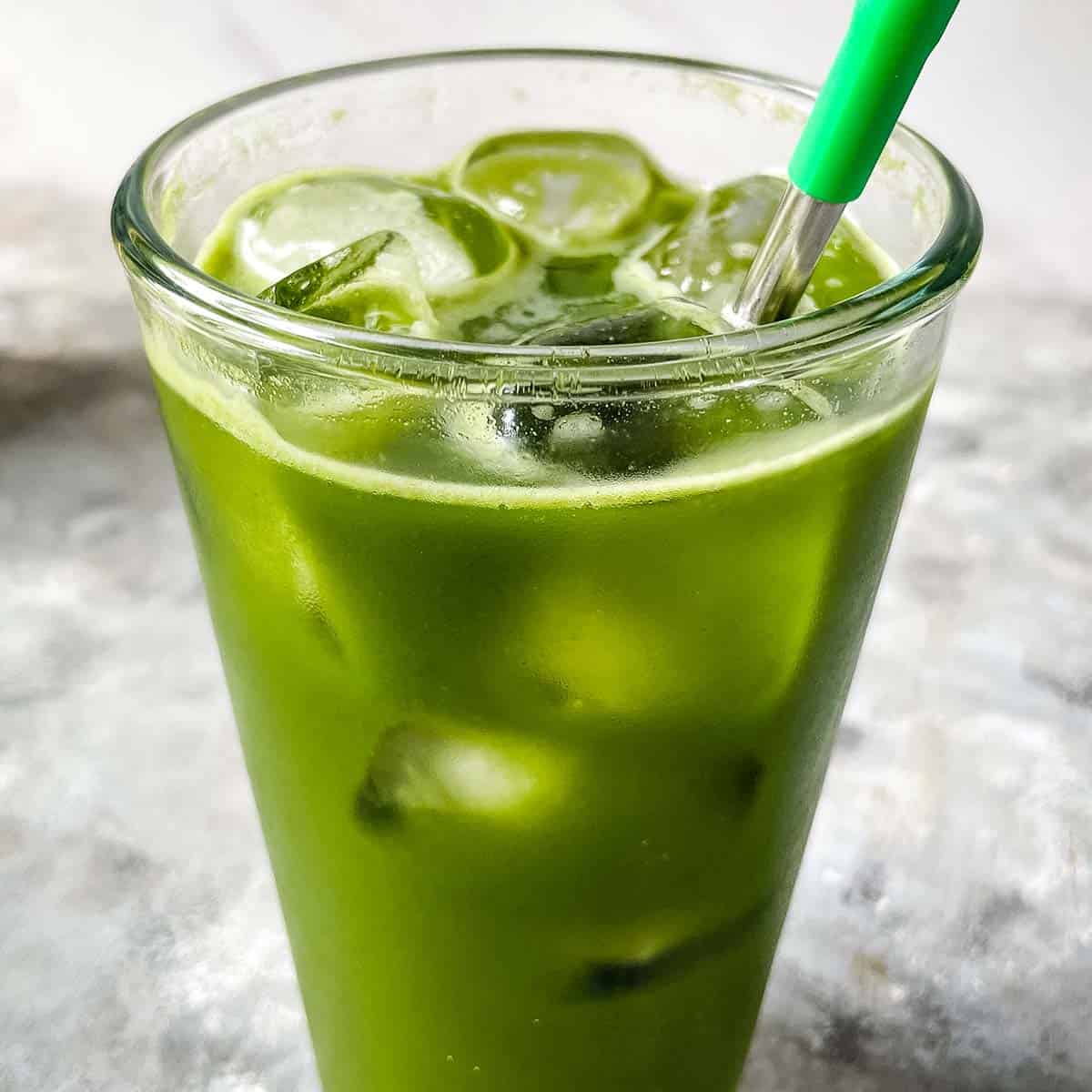 sparkling apple matcha in tall glass with ice cubes and metal straw with green silicone tip