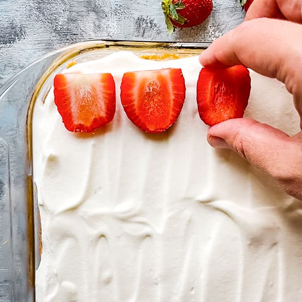 tres leches cake topped with whipped cream and strawberry halves