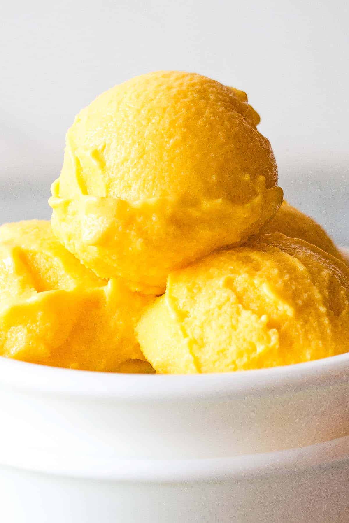 close up of mango yogurt ice cream scoops in small white bowl