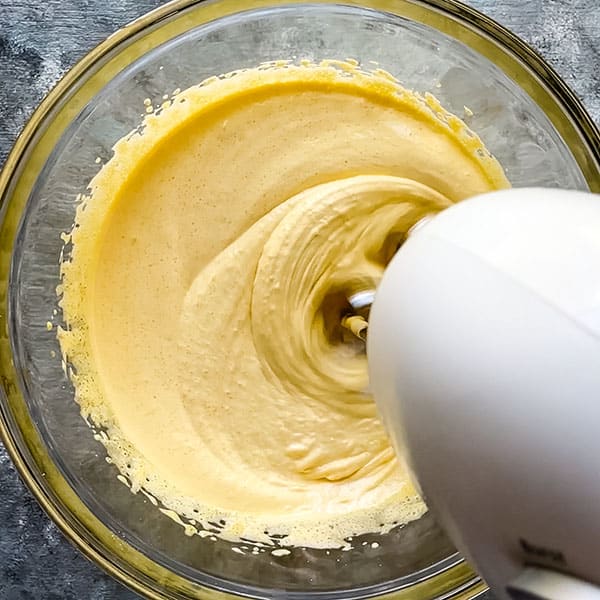 hand mixer combining egg yolks and sugar into pale yellow mixture