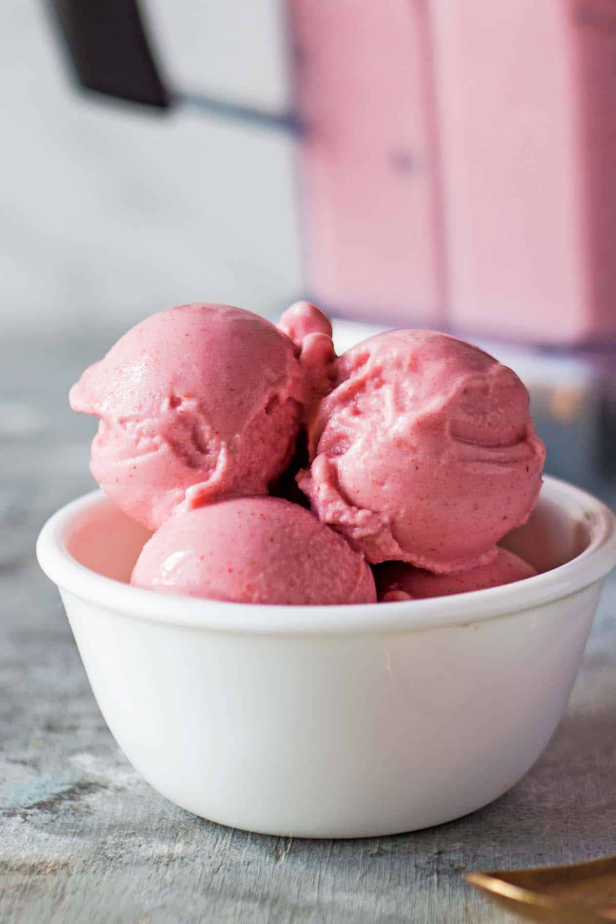 strawberry yogurt ice cream scoops in white bowl; blender in background
