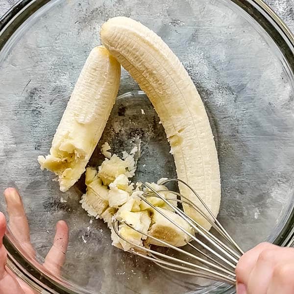 wire whisk mashing ripe bananas in large glass bowl