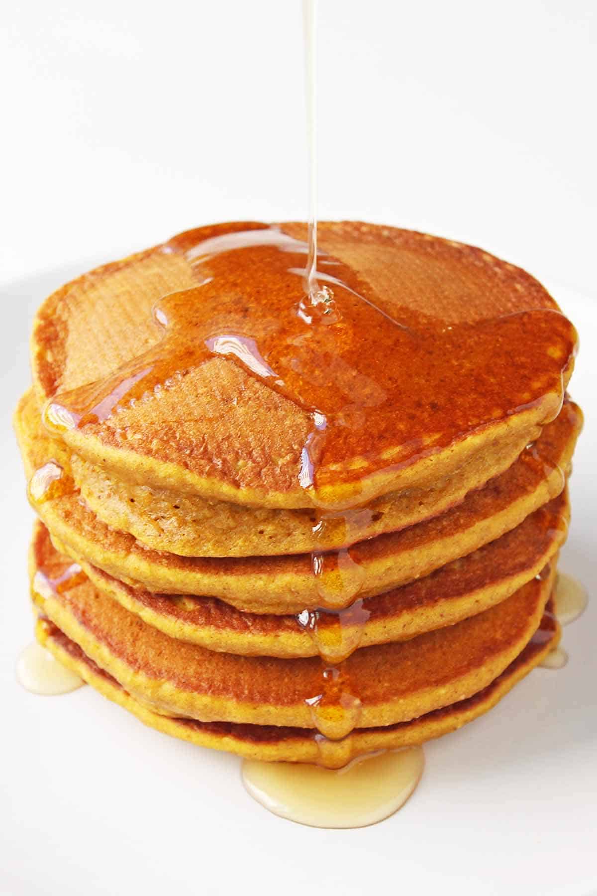 stack of pumpkin pancakes with maple syrup drizzling on top