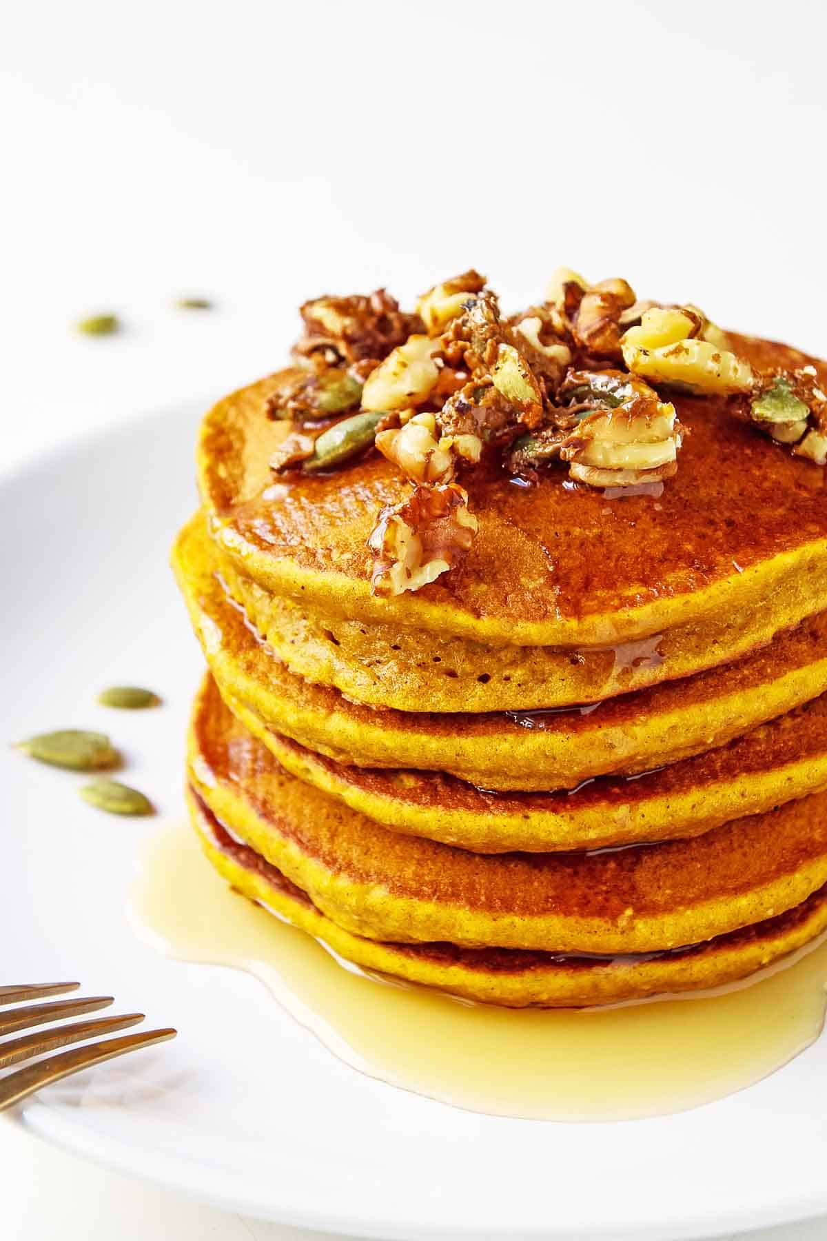 healthy pumpkin pancakes stacked on white plate with golden fork on the side