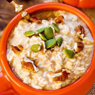 close up of overnight oats with pumpkin and pepita pecan topping in orange mug
