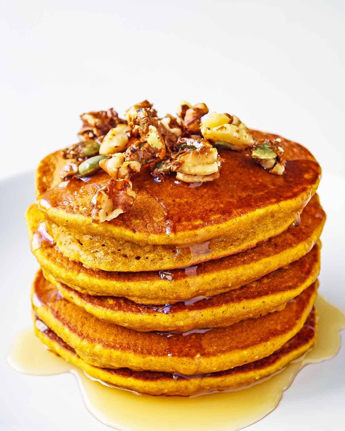 stack of healthy pumpkin pancakes with syrup drizzle and crunchy walnut pumpkin seed topping