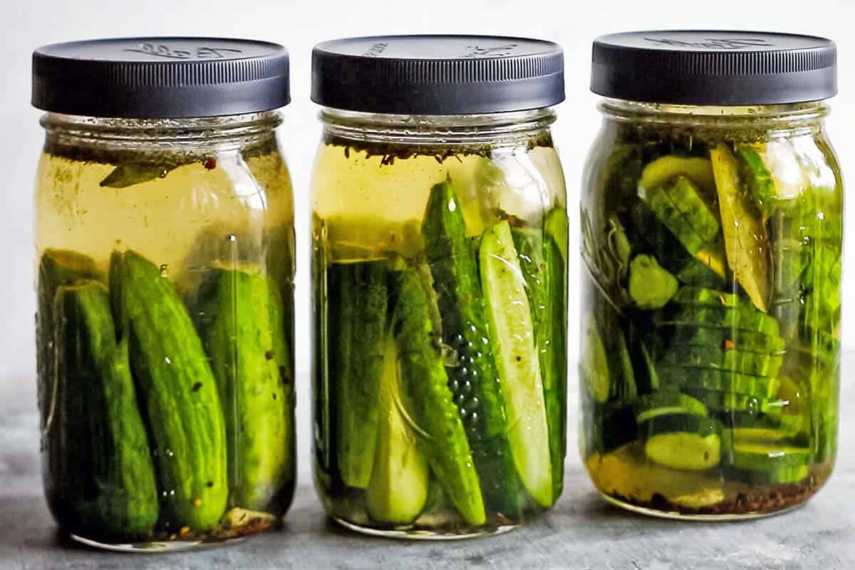 3 glass jars with whole, spears and sliced fermented pickled cucumbers