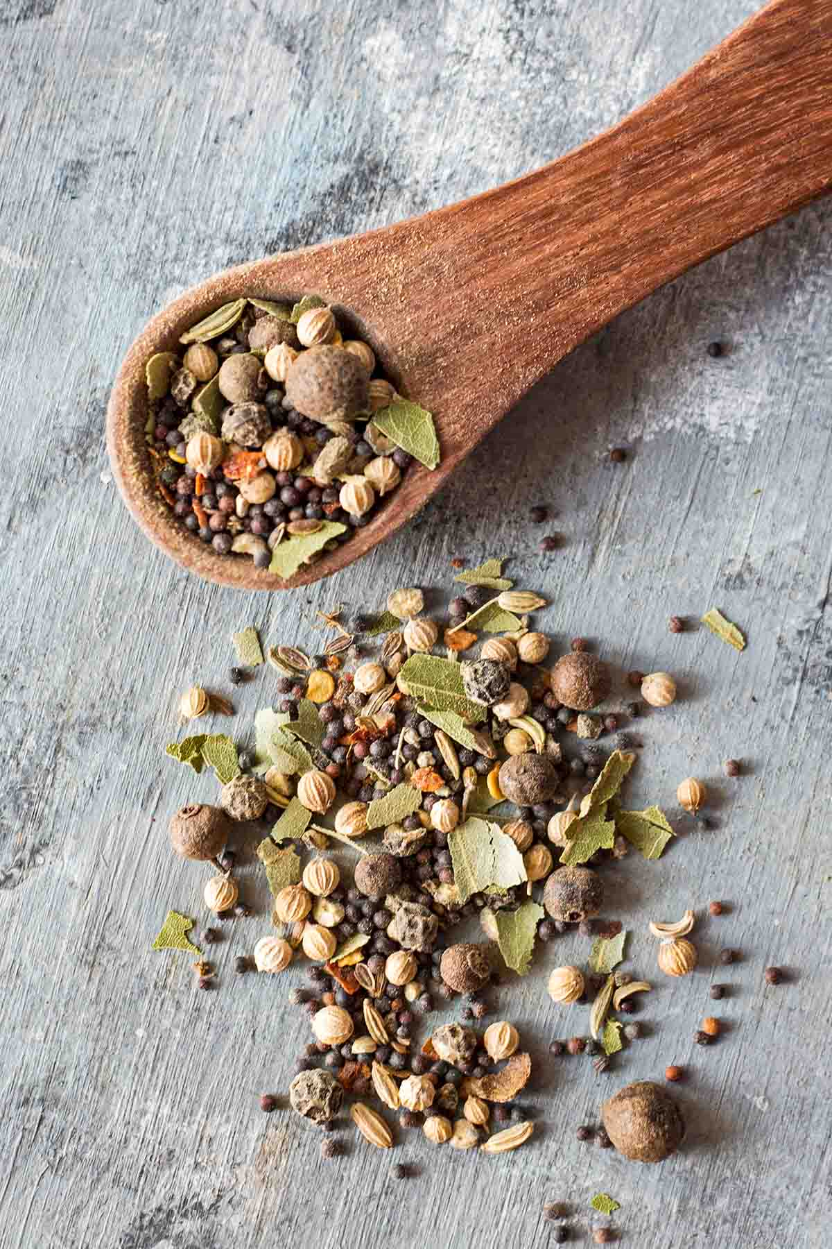 pickling spices on small wooden measuring spoon and spread on grey background
