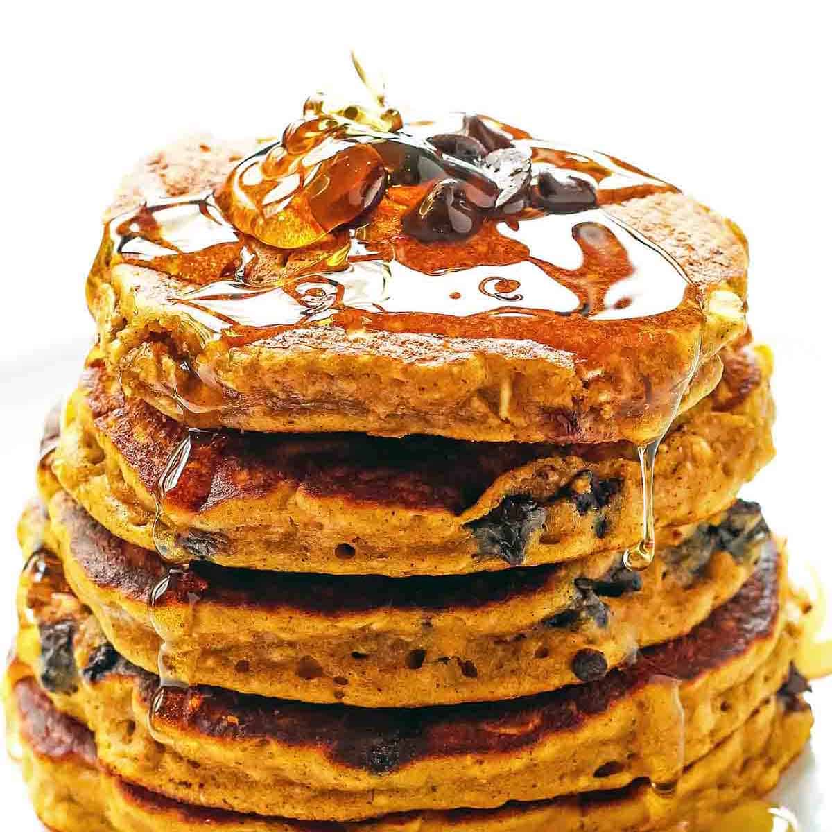 stack of pumpkin oatmeal pancakes with chocolate chips and syrup drizzle on top